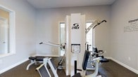 This single-floor fitness space is thoughtfully designed to provide a dedicated environment for strength training and exercise. The room features professional-grade Cybex multi-station gym equipment as its centerpiece, offering a variety of resistance training options including a lat pulldown, cable attachments, and adjustable benches — making it suitable for full-body workouts. The space is finished with neutral gray walls and carpeted flooring, contributing to a clean and functional aesthetic. Natural light filters in through multiple windows, brightening the room and creating an open, energizing atmosphere. The layout allows for ample movement around the equipment, ensuring a safe and practical workout environment. The overall design balances utility with comfort, making this fitness space a well-appointed facility for those seeking a convenient and capable place to train.