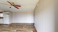 Located at 191 Railroad St in Enigma, GA, this single-floor home offers three bedrooms, two bathrooms, and a practical, efficiently organized layout. The exterior features beige vertical panel siding with white skirting, a small entry staircase with railing, and sits on a grassy lot with open views of the surrounding neighborhood.

Inside, wood-look plank flooring runs throughout, providing a cohesive and easy-to-maintain surface across all rooms. The combined kitchen and living area forms the heart of the home. The kitchen is equipped with white shaker-style cabinetry, a double-basin sink, laminate countertops, and a striking faux-stone mosaic tile backsplash that adds a decorative focal point. A window above the sink brings in natural light.

The three bedrooms feature the same durable wood-look flooring, neutral gray wall panels, and textured ceilings. The primary bedroom includes a ceiling fan, while the additional bedrooms each offer windows with blinds for natural light and privacy. The layout is straightforward and functional, with a hallway connecting the bedrooms to the rest of the home.

The two bathrooms include at least one with a full tub-shower combination and standard fixtures. Additional spaces include a dedicated laundry area and a closet for storage. The home's open surroundings provide pleasant, rural views from multiple entry points.