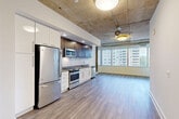 Located at 4501 Ford Ave in Alexandria, VA, this 2-bedroom, 3-bathroom residence offers a thoughtfully designed single-floor layout with a compelling blend of industrial and modern aesthetics. The open-concept living, dining, and kitchen area serves as the heart of the home, highlighted by striking exposed concrete ceilings, a ceiling fan, and expansive floor-to-ceiling windows that flood the space with natural light and frame views of the surrounding cityscape. Wide-plank hardwood-style flooring runs throughout, lending warmth and continuity to the interior. The kitchen is well-appointed with stainless steel appliances—including a refrigerator, range, microwave, and dishwasher—complemented by a two-tone cabinet scheme featuring rich dark-wood uppers and crisp white lowers, set against a clean tile backsplash. A hallway connects the private areas of the home, where two bedrooms each feature ceiling fans and closet space. The generously sized primary bedroom includes a dedicated closet and an en-suite bathroom with a sleek vanity and glass-enclosed shower. Additional bathrooms offer tiled tub-shower combinations with neutral taupe tile surrounds. The unit also includes a laundry room and utility room, providing practical everyday convenience throughout.