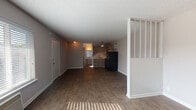 Located at 1020 Thompson Pl in Nashville, TN, this single-floor unit offers a straightforward, functional layout with consistent wood-look flooring extending throughout the space. The main living area is open and generously proportioned, with natural light filtering in through blinds-fitted windows. A textured ceiling runs across the unit, and clean white baseboards frame each room.

A distinctive architectural detail — a white partial-wall divider with vertical slat openings and built-in shelving — visually separates portions of the living space while maintaining an open feel. The kitchen is positioned toward the rear of the unit and features light wood-toned cabinetry, a single-basin sink, a ceiling fan with light fixture, and black appliances including a refrigerator and range. An over-range exhaust hood and upper cabinetry provide practical storage.

The bathroom includes a vanity with a speckled countertop, a standard toilet, and a tub-shower combination with a curtain rod. Dark wood-look flooring continues into the bathroom, maintaining visual cohesion. The unit's neutral gray and white palette throughout provides a clean, move-in ready foundation. The front entry door opens directly into the main living area, providing straightforward access.