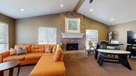 Located at 7100 Almeda Rd in Houston, TX, this single-floor community space offers a warm and functional environment designed for comfort and convenience. The centerpiece of the space is a well-appointed living room highlighted by dramatic vaulted ceilings with exposed wood beams that lend a sense of architectural character and openness. A full-height brick fireplace with a classic white mantel serves as a striking focal point, flanked by windows dressed with white blinds that allow natural light to fill the room. Plush carpeted flooring runs throughout, adding warmth underfoot. A pass-through service window with a granite ledge connects to an adjacent area, enhancing the functional flow of the space. A glass-panel entry door invites natural light into the entryway, which is accented by neutral taupe walls and tasteful décor. A secondary seating area features large windows on multiple walls, recessed lighting, and ample room for relaxed gatherings. Completing the layout is a dedicated package locker room, equipped with a modern automated locker system offering secure, convenient parcel retrieval. Together, these areas create a practical and inviting community hub well-suited for residents of the surrounding Houston neighborhood.