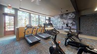 This single-story fitness center in Nashville, Tennessee is thoughtfully designed to accommodate a full range of workout disciplines across several distinct zones. The cardio area features multiple treadmills and stationary bikes, including Peloton and Matrix models, positioned alongside large windows that allow natural light to fill the space and provide views of the surrounding greenery. A bold, urban-themed mural with graphic typography serves as a dynamic focal point on one wall, reinforcing the energetic atmosphere.

The strength training zone is well-appointed with a cable machine system, weight racks, adjustable benches, and a comprehensive dumbbell collection organized on tiered racks. Built-in wooden cubbies display a full range of medicine balls and stability equipment, keeping the space orderly and accessible. Large mirrors line the walls, enhancing the sense of openness throughout.

A dedicated functional training room features hardwood flooring, spin bikes, and a well-stocked rack of kettlebells in varying weights, along with yoga mats and resistance tools. A wall-mounted display provides on-demand workout programming. Throughout the facility, recessed and linear LED lighting maintains a focused, professional ambiance. A lounge-style entry corridor with warm wood floors features a framed Nashville Predators jersey, adding a locally inspired touch.
