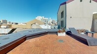 Located atop 639 Geary Street in the heart of San Francisco, this rooftop deck offers a spacious open-air retreat with striking panoramic views of the city skyline. The deck is finished with classic red brick pavers that extend across the entire surface, lending a warm and inviting character to the space.

Thoughtfully arranged seating includes woven chaise lounges positioned to take full advantage of the sweeping cityscape, along with additional seating areas featuring low benches and a round table, ideal for casual gatherings. Potted greenery and planter boxes are distributed throughout, adding a touch of nature to the urban setting.

The deck is framed by low parapet walls and architectural rooftop structures that define distinct zones within the space. A dedicated access door with an illuminated exit sign provides convenient entry and exit. The open sky above ensures abundant natural light throughout the day, while views of prominent downtown San Francisco buildings — including high-rises and historic architecture — create a dynamic urban backdrop. The overall ambiance is one of an elevated urban oasis, well-suited for relaxation or social gatherings in the midst of the city.