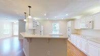 This single-story home in Columbus offers a well-designed layout across a generous footprint, providing ample space for both everyday living and entertaining. The kitchen serves as a central highlight, featuring crisp white cabinetry with glass-front upper panels, light countertops, a large wraparound peninsula with bar seating, recessed lighting, pendant fixtures, and white appliances including a double wall oven, built-in microwave, and refrigerator. Hardwood flooring runs throughout the kitchen and adjoining living area, which benefits from multiple windows that bring in natural light and views of surrounding greenery. Crown molding adds a finishing detail to the living space. The three bedrooms are carpeted and each equipped with a ceiling fan and windows overlooking the outdoors, creating comfortable, well-lit retreats. The full bathroom features tile flooring, a double-sink vanity with white cabinetry, and a full tub-shower combination. Throughout the home, a neutral color palette of warm beiges and whites creates a clean, cohesive aesthetic. Textured ceilings are consistent throughout, contributing to the home's traditional character.