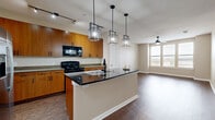 Located at 225 Town Center Lane in Keller, Texas, this single-story residence offers a well-designed open-concept layout that connects the kitchen and living areas seamlessly. The kitchen serves as the focal point of the main living space, showcasing warm wood-toned cabinetry, granite countertops, and a striking center island topped with a dark stone surface. Three geometric pendant lights hang above the island, adding a contemporary touch. Black appliances, including a gas range and built-in microwave, complement the design, while a stainless steel refrigerator anchors one end of the kitchen. Track lighting above provides additional illumination throughout the cooking area.

Rich hardwood-style flooring extends through the kitchen, living, and dining areas, contributing to a cohesive aesthetic. The living area benefits from natural light through large windows, and a ceiling fan adds both function and style. The bedrooms are generously sized, featuring plush carpeting, ceiling fans, and ample natural light—one bedroom includes floor-to-ceiling windows with outdoor views. The bathrooms are finished with white tile surrounds, soaking tubs, and hardwood-style flooring, offering a clean, functional design throughout.
