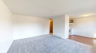 Located at 11020 16th Ave SW in Seattle, WA, this one-bedroom, one-bathroom unit offers a practical and well-organized single-floor layout. The living room is a bright, open space featuring neutral carpet, a baseboard heater, and a textured ceiling, flowing naturally into the adjacent dining area. The kitchen is equipped with gray cabinetry, a tile backsplash, wood-style flooring, a white electric range, and a refrigerator, all brightened by a skylight-style overhead fixture. A hallway connects the main living areas to the private spaces, providing a clear sense of separation. The bedroom is a comfortable, carpeted room with a sliding double-door closet, a baseboard heater, and a window that brings in natural light. Two additional closets throughout the unit offer generous storage capacity. The bathroom includes a tub-shower combination, a toilet, and a vanity with a countertop. Baseboard heating is present throughout the unit, ensuring consistent warmth. The consistent use of neutral tones, carpet in living and sleeping areas, and wood-style flooring in the kitchen and bathroom creates a cohesive and clean aesthetic throughout the space.