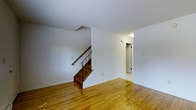 This two-bedroom, two-bathroom townhouse at Willowcrest offers a straightforward, functional layout spread across two floors. The main level features warm hardwood flooring that extends throughout the open living area, giving the space a cohesive and inviting feel. White walls and a clean, neutral palette keep the interior bright and adaptable to a variety of furnishing styles.

A staircase with rich wood treads and a classic iron railing serves as a central architectural element on the main floor, connecting the two levels while adding a touch of character to the otherwise understated design. Adjacent to the staircase, a doorway leads to an additional room or hallway, providing practical flow between spaces.

The open layout of the main level allows for flexible use of the living area, with ample wall space and room for a variety of furniture arrangements. The ceiling height contributes to an airy atmosphere throughout.

The second floor houses the two bedrooms and provides separation between the living and sleeping areas—a hallmark of townhouse-style living. With two full bathrooms distributed across the home, this townhouse at Willowcrest offers comfort and practicality for its residents.