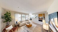 This thoughtfully designed single-floor residence offers 1 bedroom and 2 full bathrooms within a compact yet efficient layout. The open-concept living, dining, and kitchen area forms the heart of the home, bathed in natural light from large windows dressed with sheer white curtains and horizontal blinds. Light-toned hardwood-style flooring flows throughout the main living areas, lending warmth and continuity to the space.

The galley-style kitchen features white cabinetry, stone-look countertops with a double stainless steel sink, and stainless steel appliances including a refrigerator, range, and microwave. A dedicated dining area comfortably accommodates a round table and sits adjacent to a window overlooking greenery outside.

The bedroom is carpeted for comfort and includes a ceiling fan, a window with sheer curtains for soft natural light, and a dedicated closet. Two full bathrooms serve the unit, one of which includes a tub-shower combination with tile surround and hardwood-style flooring.

A dedicated laundry room houses a full-size washer and dryer alongside a water heater, adding everyday convenience. Neutral warm-beige walls throughout create a calm, cohesive ambiance, making this a practical and inviting space.