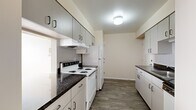 This single-floor unit offers a practical and efficiently designed layout across a modest footprint. The galley-style kitchen is a standout feature, equipped with ample white cabinetry on both sides, dark granite-style countertops, white appliances including a coil-top electric range and refrigerator, and a tile backsplash. Wood-look plank flooring runs throughout the kitchen and connecting hallways, lending a clean, cohesive aesthetic.

The layout includes two hallways that guide residents through the unit, connecting the kitchen and entry areas to the private spaces beyond. The spacious living area features neutral carpet and multiple windows fitted with blinds, allowing generous natural light to fill the room. A pendant light fixture adds a functional design accent overhead.

The bedroom is generously proportioned, featuring plush carpeting, a large window for natural light, and a built-in closet with a hanging rod for ample storage. The full bathroom features wood-look vinyl flooring, a single-sink vanity with white cabinetry, a tiled bathtub and shower combination, and a chrome towel bar. The overall palette of warm neutrals and white trim creates a clean, move-in-ready atmosphere throughout.