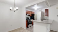 This two-floor residence offers a well-organized layout with functional design elements throughout. The kitchen serves as a central highlight, featuring warm medium-toned wood cabinetry, stainless steel appliances including a gas range and refrigerator, and a granite-style peninsula countertop with an integrated sink. The peninsula opens directly to the adjacent dining and living areas, which are finished with neutral-toned carpet and accented by a modern chandelier, creating a cohesive and welcoming common space. Built-in closet storage is visible in the living area, adding practical utility.

The bedrooms are carpeted and bright, each benefiting from large windows fitted with vertical blinds that allow natural light while maintaining privacy. The rooms offer generous wall space and a clean, neutral palette. Bathrooms are finished with tile flooring, white vanities, and full tub-shower combinations surrounded by white tile surrounds, maintaining a consistent, clean aesthetic. The overall design of the residence emphasizes clean lines, neutral tones, and practical functionality across both floors, making it a well-structured and move-in-ready space.