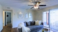 This single-floor residence offers a comfortable and thoughtfully designed living space. The living room serves as the heart of the home, featuring warm wood-style flooring that adds a rich, grounded feel to the interior. A multi-blade ceiling fan with integrated lighting anchors the room from above, providing both airflow and ambient illumination. The textured ceiling adds a classic residential character throughout.

Natural light flows generously into the living area through a sliding glass door, brightening the neutral, soft-toned walls and creating an open, airy atmosphere. A set of three framed wall prints adds a decorative focal point, complementing the understated color palette of the space.

The room is well-proportioned, offering ample space for comfortable seating and everyday living. The overall design aesthetic is clean and functional, blending neutral tones with warm wood accents for a cohesive, inviting environment. The layout and finishes suggest a space that is move-in ready and well-maintained, making it a practical and welcoming home for everyday living.