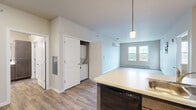 This single-floor unit offers a well-designed, open-concept layout that seamlessly connects the kitchen, dining, and living areas. The kitchen serves as a central feature, showcasing rich dark brown cabinetry with sleek hardware, white quartz-style countertops, and a full suite of black appliances including a range, microwave, dishwasher, and refrigerator. A peninsula with pendant lighting provides additional workspace and casual seating opportunities while anchoring the open living space. Wood-look plank flooring runs throughout the main living areas, adding warmth and visual continuity.

The living area is bright and airy, featuring two large windows that allow natural light to fill the room and offer outdoor views, complemented by a wall-mounted mini-split system and baseboard heating. Bedroom spaces feature plush carpeting, neutral wall tones, and individual climate controls. The bathroom is finished with a dark wood vanity, white countertop, a large mirror, wood-look flooring, and chrome fixtures. A dedicated in-unit laundry closet with a stacked washer and dryer adds everyday convenience. Throughout, the unit maintains a clean, contemporary aesthetic with neutral tones and modern finishes.