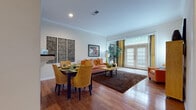 This single-floor residence is thoughtfully designed to maximize both function and comfort across its interconnected living spaces. The open-concept living and dining area serves as the heart of the home, featuring warm hardwood flooring, crown molding, and recessed lighting throughout. A set of French doors floods the space with natural light and provides outdoor access, while decorative wall art and built-in shelving add architectural interest. The dining area benefits from a pass-through window that connects directly to the galley-style kitchen, which is outfitted with white cabinetry, white appliances including a range, microwave, refrigerator, and dishwasher, and a double sink with ample counter space on both sides. The bedroom is generously sized with plush carpeting, a large window with outdoor views, and sufficient space for a full furniture arrangement. The full bathroom features an extended white vanity with a large mirror, pendant lighting, tile flooring, and a tub-shower combination. A dedicated laundry area with a washer and dryer and an electrical panel completes the layout, adding practical convenience to the residence.