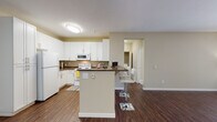 Located at 1500 White Birch Terr in Fremont, California, this single-floor residence offers a well-designed layout with a cohesive blend of function and comfort throughout. The kitchen is a standout feature, outfitted with crisp white cabinetry, dark countertops, and a full suite of white appliances including a refrigerator, electric range, and over-the-range microwave. Rich wood-look flooring runs throughout the kitchen and living areas, adding warmth and continuity to the space. A peninsula island with a dark countertop provides additional prep space and doubles as a casual dining area, accommodated by white bar-height seating. The open layout connects the kitchen seamlessly to the living area, which benefits from natural light streaming through vertical-blind-covered windows and is equipped with a ceiling fan. The bedroom features plush carpeting, neutral walls, and direct access to a closet area, creating a calm and functional retreat. The full bathroom includes a tub-shower combination with tile surround, a white vanity with dark countertop, a large mirror, and wood-look flooring. A dedicated in-unit laundry closet houses a full-size washer and dryer with overhead shelving, adding everyday convenience to this practical and well-appointed residence.