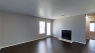 This single-story space offers a clean and functional layout with a straightforward, practical design. The main living area is a standout feature, showcasing rich, dark hardwood flooring that anchors the room with warmth and visual depth. A classic tile-surround fireplace with a black firebox insert serves as a focal point, adding a cozy and inviting element to the space. Natural light filters in through a side window and an exterior door, brightening the neutral gray walls and contributing to an open, airy feel. The textured popcorn ceiling adds a traditional touch overhead, while the white baseboards provide a crisp contrast to the darker flooring. The exterior door offers convenient outdoor access, adding to the practicality of the layout. The overall ambiance is understated and move-in ready, with a neutral color palette that allows for flexible interior styling. The combination of the fireplace, hardwood floors, and natural light creates a comfortable and welcoming living environment suited for everyday use.