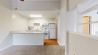 This single-floor unit offers a thoughtfully laid-out living space that maximizes functionality within a compact footprint. The open-concept design seamlessly connects the living room and kitchen, creating a cohesive and airy feel throughout.

The kitchen is a standout feature, equipped with crisp white shaker-style cabinetry that extends to the ceiling for ample storage. Light granite countertops run along the workspace and continue onto a peninsula that doubles as a breakfast bar, providing additional prep space and a natural divider between the kitchen and living area. White appliances — including a full-size refrigerator, electric range, and dishwasher — are complemented by a classic white subway tile backsplash. Hardwood flooring grounds the kitchen with warmth.

The living room is carpeted and bathed in natural light from a large window fitted with vertical blinds, offering views of surrounding greenery. The entryway, accented with a hardwood threshold, welcomes residents into the space.

The bathroom includes a full tub-shower combination with white tile surround, brushed gold fixtures, and hardwood flooring, maintaining a clean and functional aesthetic. A dedicated closet provides convenient storage to complete the unit's practical layout.