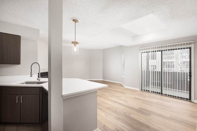 Modern apartment kitchen with elegant white countertops, stainless steel appliances, and warm wood flooring. - Avana Belmar