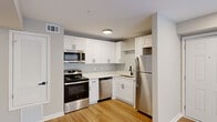 Located at 1500 Champions Pines Lane in Augusta, GA, this one-bedroom, two-bathroom residence offers a well-designed single-floor layout with modern finishes throughout. The kitchen and living room share an open, functional layout anchored by light wood-tone flooring. The kitchen is outfitted with crisp white shaker cabinets, white countertops, a subway tile backsplash, and a full suite of stainless steel appliances including a range, microwave, dishwasher, and refrigerator. A louvered utility closet adds practical storage nearby. The living area is bright and open, featuring recessed lighting and French doors that open to an outdoor patio, inviting natural light and outdoor views into the space. The bedroom is carpeted, offering a cozy retreat, and is served by a dedicated walk-in closet with rod and shelf storage. Both bathrooms are well-appointed; one features a white vanity with a vessel sink, a large mirror with modern light fixtures, and tiled flooring, complementing the clean, contemporary aesthetic found throughout. Neutral wall tones and white trim carry through each room, creating a cohesive and welcoming atmosphere well-suited to a variety of lifestyles.