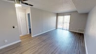This single-floor unit offers a clean, contemporary aesthetic defined by neutral gray tones, crisp white trim, and updated wood-look vinyl flooring that flows consistently throughout the space. The open living area is generously proportioned, bathed in natural light from a full sliding glass door that leads to an outdoor balcony fitted with vertical blinds. A ceiling fan adds comfort and function overhead, while a textured popcorn ceiling provides a classic finish.

The layout transitions naturally into a secondary living or dining space, connected by an open passage that maintains an airy, open feel. The galley-style kitchen is efficiently designed with white shaker cabinetry, gray quartz-style countertops, black appliances including a full-size refrigerator and dishwasher, a double stainless steel sink, and a window with vertical blinds that brings in additional natural light.

The bedroom is a comfortable retreat featuring the same wood-look flooring, neutral walls, a window for natural light, and a full mirrored sliding closet that adds depth and reflects light throughout the room. The bathroom is neatly finished with a white vanity, granite-style countertop, a tub-and-shower combination, and brushed nickel fixtures and hardware. The overall ambiance is bright, refreshed, and move-in ready.
