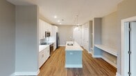 Located at 4930 Goose Creek Dr in Charlotte, NC, this single-floor residence offers a thoughtfully designed layout with modern finishes throughout. The open-concept kitchen serves as the heart of the home, showcasing crisp white shaker cabinetry, white quartz countertops, and a herringbone-patterned blue subway tile backsplash. A spacious center island with an undermount sink provides both workspace and casual dining, while two oversized clear glass pendant lights add a striking visual element. Stainless steel appliances complete the kitchen's contemporary aesthetic. Warm hardwood-style flooring flows through the main living and kitchen areas, lending a sense of continuity and warmth. The living area is bathed in natural light through large windows that offer views of the surrounding neighborhood. The bedroom features plush carpeting, a ceiling fan, and a window with outdoor views, creating a comfortable retreat. The en-suite bathroom is well-appointed with a dual-sink white vanity, a glass-enclosed walk-in shower with tile surround, and hardwood-style flooring. A generously sized walk-in closet with wire shelving provides ample storage. Neutral tones throughout create a clean, cohesive ambiance well-suited for modern living.