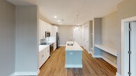 Located at 4930 Goose Creek Dr in Charlotte, NC, this single-floor residence offers a thoughtfully designed layout with modern finishes throughout. The open-concept kitchen serves as the heart of the home, showcasing crisp white shaker cabinetry, white quartz countertops, and a herringbone-patterned blue subway tile backsplash. A spacious center island with an undermount sink provides both workspace and casual dining, while two oversized clear glass pendant lights add a striking visual element. Stainless steel appliances complete the kitchen's contemporary aesthetic. Warm hardwood-style flooring flows through the main living and kitchen areas, lending a sense of continuity and warmth. The living area is bathed in natural light through large windows that offer views of the surrounding neighborhood. The bedroom features plush carpeting, a ceiling fan, and a window with outdoor views, creating a comfortable retreat. The en-suite bathroom is well-appointed with a dual-sink white vanity, a glass-enclosed walk-in shower with tile surround, and hardwood-style flooring. A generously sized walk-in closet with wire shelving provides ample storage. Neutral tones throughout create a clean, cohesive ambiance well-suited for modern living.