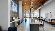 Located at 300 S Firestone St in Gastonia, NC, this thoughtfully renovated industrial space masterfully blends historic character with contemporary design. The single-floor layout offers generous, open square footage that flows seamlessly between distinct functional zones. Exposed brick walls, warm wood-plank ceilings with visible timber beams, polished concrete floors, and original round wooden columns define the architectural identity of the space throughout.

Natural light pours in abundantly through large, multi-pane factory-style windows with dark steel frames, creating a bright and inviting atmosphere. The main gathering area features a long central island with bar seating, a built-in coffee and beverage station, a wine refrigerator, and café-style banquette seating beneath a striking neon logo sign and bold dark accent wall adorned with living moss panels.

Two distinct lounge areas provide flexible seating arrangements — one with blue upholstered chairs set against raw brick walls beneath oversized arched windows, and another with leather seating and a large-screen television. A dedicated game area includes ping pong and shuffleboard tables on polished concrete floors, complemented by curated artwork. Exposed ductwork and industrial pendant lighting complete the aesthetic, reinforcing the space's dynamic, loft-inspired character.