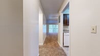 Located at 200-216 Belmont St in Liberty, Missouri, this single-floor unit offers a thoughtfully organized layout comprising a living room, bathroom, hallway, and kitchen area. The carpeted living room serves as the heart of the space, highlighted by a full-height brick fireplace with a raised hearth — a striking architectural focal point. A ceiling fan adds comfort, and a large sliding glass door fitted with vertical blinds opens to a private balcony, filling the room with natural light and offering pleasant outdoor views of surrounding trees. Adjacent to the living room, the kitchen features dark wood cabinetry, light granite-style countertops, and tile flooring, providing a practical and cohesive cooking space. A hallway connects the main living areas to the bathroom, which is finished with warm-toned tile flooring, a full tub-shower combo with white tile surround, a wood vanity with a granite-style countertop, and clean white walls. Throughout the unit, textured ceilings and neutral wall tones create a consistent, understated aesthetic. Closet storage is accessible from the living area, adding functional convenience to the overall layout.