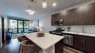 Located at 2000 Pennsylvania Ave in Wilmington, Delaware, this single-floor residence offers a thoughtfully designed open-concept layout with contemporary finishes throughout. Rich dark hardwood flooring flows seamlessly across the living, dining, and kitchen areas, grounding the space with warmth and continuity.

The kitchen is a standout feature, equipped with stainless steel appliances including a gas range, built-in microwave, and dishwasher. Dark espresso cabinetry pairs with a crisp white quartz countertop and subway tile backsplash, while a central island with bar seating serves as an ideal gathering point. Stylish pendant lighting completes the look.

The open living area is bright and inviting, anchored by large sliding glass doors that lead to a private balcony overlooking a landscaped courtyard. The outdoor space is framed by mature trees and neighboring architectural elements, providing a pleasant urban retreat.

The bedroom is generously proportioned, featuring large windows with courtyard views, dark hardwood floors, and direct access to a walk-in closet area. The bathroom maintains the same design language with dark cabinetry, a white quartz vanity, a framed mirror, and a tall storage cabinet, offering both style and functionality. The overall ambiance is modern, clean, and well-appointed.