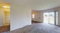 This single-floor unit offers a thoughtfully designed layout that balances comfort and functionality throughout. The expansive living area is finished with plush wall-to-wall carpeting and crisp white walls, creating a bright and welcoming atmosphere. A sliding glass door opens directly to a private balcony, allowing an abundance of natural light to fill the space while providing outdoor views of the surrounding area. A secondary window further enhances ventilation and daylight.

The kitchen is a standout feature, showcasing rich dark wood cabinetry with sleek brushed-nickel hardware, granite-look countertops, and a classic white subway tile backsplash. Stainless steel appliances — including a dishwasher, electric range, and over-the-range microwave — complete this well-equipped culinary space, finished with durable hardwood-style flooring.

The bedrooms are generously sized, each with soft carpeting and ample natural light from multiple windows fitted with blinds. The bathroom features neutral tile flooring, white tile wainscoting, a dark vanity with a white countertop, and clean, functional fixtures. The overall palette of neutral tones and consistent finishes throughout the unit creates a cohesive and move-in-ready environment.