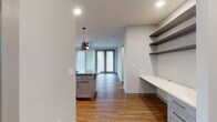 This single-floor residence showcases a thoughtfully designed open-concept layout with consistent wood-look flooring connecting the living spaces. The kitchen serves as a central highlight, featuring gray shaker-style cabinetry extending to the ceiling, white quartz countertops, a full suite of stainless steel appliances including a French door refrigerator, electric range, and microwave. A large center island with a contrasting gray countertop provides additional workspace and casual seating, illuminated by two modern pendant lights.

Adjacent to the kitchen, a dedicated built-in workspace features a long white desk surface and multiple open shelving units, ideal for a home office setup. The living area offers generous space with a ceiling fan, recessed lighting, and floor-to-ceiling glass doors that invite natural light.

The bedrooms are well-proportioned, each equipped with ceiling fans and large windows fitted with horizontal blinds. The primary bathroom features warm wood-toned cabinetry, a glass-enclosed shower, white tile flooring, and direct access to a spacious walk-in closet with built-in shelving. A secondary bathroom mirrors the clean aesthetic with subway-tiled tub surround and matching wood vanity.