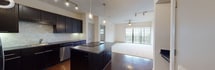 This single-floor apartment in Dallas's 75208 zip code offers a thoughtfully designed open-concept layout. The kitchen is equipped with dark espresso cabinetry, stainless steel appliances, a tiled backsplash, and a central island with a built-in cooktop, illuminated by stylish pendant and track lighting. The spacious living area features hardwood flooring transitioning to plush carpet, a ceiling fan, and large sliding glass doors that invite abundant natural light and outdoor views. The carpeted bedrooms include ceiling fans and windows with blinds. Bathrooms are finished with dark vanities, stone countertops, glass-enclosed showers, and large-format tile flooring.