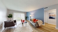 Located at 9920 Grace Dr in Port Richey, Florida, this single-floor home offers a well-designed layout with a warm, modern aesthetic throughout. The living area is a welcoming focal point, showcasing light wood-style flooring, a bold blue accent wall, and a large sliding glass door fitted with vertical blinds that invite natural light and offer pleasant outdoor views. An open sightline connects the living space to a dedicated dining area, which features a granite-topped breakfast bar with seating. The kitchen is a standout, boasting rich dark wood cabinetry, granite countertops, a decorative mosaic tile backsplash, stainless steel appliances, and a skylight that bathes the space in natural light. Tile flooring completes the kitchen's clean, practical finish. The bedrooms are comfortably sized, each featuring light wood flooring, sliding closet doors, and a neutral color palette that promotes a calm atmosphere. The bathroom is finished with beige tile surround in the tub-shower combination, a white vanity with ample storage, and coordinating tile flooring. Throughout the home, consistent light wood flooring, clean white baseboards, and a cohesive neutral color scheme create a bright, inviting ambiance suited for comfortable Florida living.