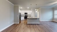 Located along US-64 E in Pittsboro, NC, this single-story home offers a thoughtfully designed layout that balances modern finishes with functional living spaces. The open-concept kitchen serves as the heart of the home, showcasing white shaker-style cabinetry, granite countertops, a classic subway tile backsplash, and a full suite of stainless steel appliances including a refrigerator, range, and microwave. A kitchen island with pendant lighting provides additional prep space and flows seamlessly into the main living area, which features warm hardwood-style flooring and crown molding throughout. The bedrooms are carpeted for comfort and bathed in natural light through sizable windows fitted with blinds. Each room includes a ceiling fan and generous closet space, with at least one bedroom offering a walk-in closet with built-in hanging rods. The bathrooms are consistently finished with dark espresso vanity cabinetry, granite countertops, and full tub-shower combinations set against clean white surrounds, all laid over light ceramic tile flooring. Neutral gray tones carried throughout the home create a cohesive, move-in-ready aesthetic suited for a variety of lifestyles.