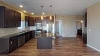 Located at 5000 28th Ave S in Fargo, North Dakota, this single-floor unit offers a thoughtfully designed layout with modern finishes throughout. The kitchen is a standout feature, showcasing rich dark espresso cabinetry, granite countertops, a subway tile backsplash, and a full suite of stainless steel appliances including a refrigerator, range, microwave, and dishwasher. A central island with pendant lighting above provides additional prep space and anchors the kitchen's open feel. Wood-look flooring flows seamlessly from the kitchen into the dining and living areas, where recessed lighting and large windows allow natural light to pour in throughout the day. The living area connects to an exterior door, offering convenient outdoor access. Bedrooms are finished with plush carpet and feature windows with blinds that provide both natural light and privacy, along with closet storage. The bathroom continues the space's cohesive aesthetic with dark cabinetry, granite countertops, an undermount sink, a large frameless mirror, and wood-look flooring. Neutral wall tones throughout the unit create a warm, inviting ambiance that complements the contemporary finishes, making this a well-balanced and functional living space.