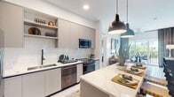 This well-designed single-floor residence offers two bedrooms and two bathrooms within a thoughtfully planned layout. The contemporary kitchen serves as a central highlight, featuring flat-front cabinetry in a warm gray tone, white subway tile backsplash, stainless steel appliances, and a quartz-topped island illuminated by bold industrial pendant lights. The open sightlines connect the kitchen directly to the living area, which features large sliding glass doors that invite natural light and provide access to an outdoor balcony with exterior views.

The primary bedroom is a comfortable retreat with direct access to a well-equipped en-suite bathroom. This bathroom features a dual-sink vanity with a white quartz countertop, LED-backlit mirrors, gray cabinetry, and a glass-enclosed walk-in shower with floor-to-ceiling tile. A spacious walk-in closet with built-in shelving and hanging rods provides practical storage. The second bathroom follows a similarly refined design aesthetic. Both bedrooms feature light-toned flooring that extends throughout the residence, contributing to a bright, cohesive atmosphere. Light neutral walls and recessed lighting further enhance the clean, modern character of the space.