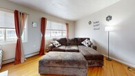 Located on Monroe Ave in Rochester, NY, this 2-bedroom, 1-bathroom single-floor unit offers a practical and well-organized layout. The entrance opens into a hallway that flows naturally into the main living areas, all connected by warm, honey-toned hardwood floors throughout.

The combined dining and living room serves as the heart of the unit. The dining area is brightened by a large window framing outdoor greenery, with an elegant chandelier overhead. The living room features ample natural light, a sectional sofa, and windows overlooking the exterior.

The galley-style kitchen provides generous cabinetry with warm wood tones, a full suite of appliances including an electric range and refrigerator, and a window for added natural light. Storage and counter space run along both sides of the kitchen corridor.

The primary bedroom is notably spacious and features hardwood floors, baseboard heating, and bold Van Gogh-inspired décor including wall art, curtains, and a rug. The second bedroom is cozily appointed with string lights lining the ceiling perimeter and blackout curtains.

The bathroom features a retro pink tile aesthetic with wainscoting, a combined tub and shower with sliding doors, a large vanity, and white tile flooring. The unit also includes a hallway with a closet near the entrance, adding convenient storage.