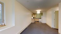 Located at 2 Gile Hill in Hanover, New Hampshire, this single-floor unit offers a straightforward and functional layout designed for comfortable everyday living. The open floor plan seamlessly connects the living area to the kitchen, creating a cohesive and efficient use of space. The living area features neutral-toned carpet flooring and clean, cream-colored walls, contributing to a bright and understated atmosphere. Baseboard heating runs along the perimeter, ensuring consistent warmth throughout. The kitchen is well-appointed with light wood cabinetry, a dark countertop, a stainless steel sink, and a full-size white refrigerator. A dishwasher and additional under-counter appliances are also present, making the kitchen highly functional for daily use. An accent wall in a muted sage green adds a subtle touch of color to the kitchen area, while a flush-mount ceiling light provides focused illumination over the space. The smooth white ceiling and recessed lighting in the living area further enhance the clean, modern aesthetic of the unit. Overall, the space presents a practical and well-maintained environment suited for a variety of occupants.