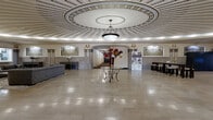 Located at 278 Main St in West Haven, Connecticut, this impressive single-floor space showcases remarkable Beaux-Arts architectural heritage across a generously proportioned open layout. The centerpiece of the space is a breathtaking coffered rotunda dome, adorned with radiating plasterwork and a central pendant light fixture that bathes the room in warm, even illumination. Polished marble tile flooring extends throughout, reflecting light and reinforcing the sense of grandeur.

Ornate classical detailing is present at every turn — gilded laurel wreath motifs, elegant cornices, and decorative friezes run along the upper walls, while fluted marble pilasters frame archways and wall niches with stately authority. Arched stained glass windows allow soft, diffused natural light to filter into the space, complementing the building's historic character.

The layout flows through a series of interconnected areas, including a welcoming rotunda seating area furnished with upholstered sofas and lounge chairs, a vestibule entry corridor with marble wainscoting, and a secondary seating alcove. A bank of modern parcel lockers occupies one wall alongside the stained glass windows, blending contemporary utility with historic surroundings. The overall ambiance is one of timeless civic elegance, combining preservation of classical architecture with thoughtful modern functionality.