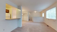 This three-floor property offers a thoughtfully designed layout with distinct functional zones spread across its levels. The upper floor, visible in the image, showcases an open-concept space finished with plush wall-to-wall carpeting in a neutral beige tone, lending a warm and comfortable feel to the area. Crisp white walls and a clean white ceiling contribute to a bright, airy atmosphere, further enhanced by a window that allows natural light to filter into the space.

A built-in pass-through counter with a granite-style surface defines one side of the upper level, creating a practical dividing element between areas while maintaining visual openness. Structural columns add architectural character without interrupting the flow of the space. A set of bi-fold closet doors provides convenient built-in storage, while a staircase connects this level to the floors below, reinforcing the multi-story nature of the property. Ceiling-mounted light fixtures ensure consistent illumination throughout. The overall ambiance is clean, neutral, and move-in ready, offering a versatile canvas suitable for a variety of uses.
