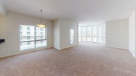 This single-floor unit presents a thoughtfully designed layout with a variety of finishes and functional spaces distributed across multiple rooms. The kitchen serves as a central highlight, featuring white shaker-style cabinetry, dark granite countertops, stainless steel appliances including a gas range, built-in microwave, and dishwasher, along with open shelving and a window that brings in natural light and exterior views. The counters offer generous prep space, making this kitchen both practical and visually appealing.

The living area is spacious and carpeted, with large floor-to-ceiling windows that allow abundant natural light to fill the room, creating an open and airy atmosphere. The bedrooms are similarly finished with neutral-toned carpet and feature closets and windows fitted with blinds.

The hallways and corridors are finished with rich, dark hardwood-style flooring and illuminated by recessed ceiling lights, giving these transitional spaces a polished, clean appearance. A utility access panel is also visible along one corridor wall.

The bathrooms feature large-format tile flooring, soaking tubs with tiled surrounds, and clean, neutral finishes throughout, providing a calm and functional environment. The overall design aesthetic is consistent and modern, with a neutral color palette unifying the entire space.