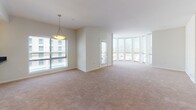 This single-floor unit presents a thoughtfully designed layout with a variety of finishes and functional spaces distributed across multiple rooms. The kitchen serves as a central highlight, featuring white shaker-style cabinetry, dark granite countertops, stainless steel appliances including a gas range, built-in microwave, and dishwasher, along with open shelving and a window that brings in natural light and exterior views. The counters offer generous prep space, making this kitchen both practical and visually appealing.

The living area is spacious and carpeted, with large floor-to-ceiling windows that allow abundant natural light to fill the room, creating an open and airy atmosphere. The bedrooms are similarly finished with neutral-toned carpet and feature closets and windows fitted with blinds.

The hallways and corridors are finished with rich, dark hardwood-style flooring and illuminated by recessed ceiling lights, giving these transitional spaces a polished, clean appearance. A utility access panel is also visible along one corridor wall.

The bathrooms feature large-format tile flooring, soaking tubs with tiled surrounds, and clean, neutral finishes throughout, providing a calm and functional environment. The overall design aesthetic is consistent and modern, with a neutral color palette unifying the entire space.