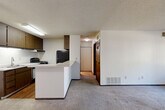 Located at 3688 Parkmoor Village Dr in Colorado Springs, CO, this one-bedroom, one-bathroom unit is thoughtfully laid out across a single floor. The kitchen features dark wood cabinetry extending to the upper walls for generous storage, light countertops, wood-look flooring, and black appliances including a gas range and refrigerator. A built-in breakfast bar peninsula connects the kitchen to the combined dining area, creating an open, functional flow. The carpeted living room is bright and open, highlighted by a ceiling fan and a sliding glass door that leads to a private patio with outdoor views. A hallway connects the main living areas to the bedroom and bathroom, with four closets throughout providing notable storage capacity. The bedroom is comfortably sized, featuring plush carpet, a sliding double-door closet, a window with vertical blinds for natural light, and wall-unit climate control. The full bathroom offers wood-look flooring, a single vanity with under-sink storage, a full tub-shower combo, and clean white finishes throughout. A utility room and textured ceilings are consistent throughout the unit, contributing to its functional, straightforward character.