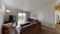 Located at 4333 Bayberry Cove in Bellbrook, Ohio, this single-floor residence offers a practical and comfortable layout across several well-defined living spaces. The living room serves as the central gathering area, featuring vaulted ceilings that lend a sense of openness, neutral carpet flooring, and a sliding glass door with vertical blinds that provides direct access to an outdoor deck and invites generous natural light. The galley-style kitchen is efficiently designed with wood-toned cabinetry, a gas range, white refrigerator, and a double sink. A hallway off the kitchen leads to a dedicated laundry area with a full-size washer and dryer, along with an electrical panel conveniently housed in the same space. Wood-look flooring runs through the kitchen and utility areas. The bedroom features carpet flooring and access to a spacious walk-in closet with built-in rod storage. Two full bathrooms are present in the home, each with a vanity, single-basin sink, and shower-tub combination. The overall layout, as reflected in the overhead floor plan view, is compact yet functional, making efficient use of the available space throughout.