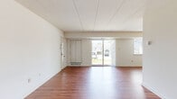 This single-floor residence offers a straightforward, functional layout with a clean, neutral palette throughout. The open living area makes an immediate impression with its rich, warm-toned hardwood-style flooring, crisp white walls, and a panel ceiling that runs the length of the space. A sliding glass door at the far end of the living area floods the room with natural light and provides direct outdoor views, while a secondary window further enhances brightness. A built-in storage unit and a wall-mounted heating vent add practical utility to the space.

The kitchen is efficiently designed with warm wood cabinetry, a tile backsplash, and tile flooring. It is fully equipped with black appliances, including a gas range, over-the-range microwave, dishwasher, and a full-sized refrigerator.

The bedrooms feature neutral carpet flooring and are brightened by windows overlooking the surrounding greenery. Each room offers a comfortable sense of space with clean white walls and structural beam details.

Two bathrooms serve the unit. The primary bathroom features a dual-sink vanity with a white countertop, wood cabinetry, and a mirrored medicine cabinet. The secondary bathroom offers a single-sink vanity with similar cabinetry and a mirrored cabinet above.