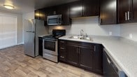 This single-floor unit offers a thoughtfully designed layout that balances functionality and comfort. The living area is a standout space, featuring rich wood-look laminate flooring and a large vertical-blind sliding door that floods the room with natural light, creating an open and airy atmosphere. A textured ceiling adds a classic architectural detail throughout the common areas and bedrooms.

The kitchen is well-equipped and modern, showcasing sleek dark espresso cabinetry that extends to the ceiling for ample storage, light speckled countertops, and a full suite of stainless steel appliances including a refrigerator, gas range, built-in microwave, and dishwasher. Wood-look flooring continues seamlessly from the living area into the kitchen, tying the spaces together cohesively.

The entryway provides a welcoming transition into the unit, complete with a double-door closet for convenient storage. The bedrooms are finished with plush wall-to-wall carpeting and feature vertical blind-covered windows that allow for natural light while maintaining privacy.

The bathroom is clean and functional, appointed with light wood-look vinyl flooring, a full tub-shower combination with chrome fixtures, and a dark-cabinet vanity with a granite-style countertop, offering a polished and practical finish.