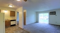 This single-floor residence offers a straightforward and functional layout designed for comfortable everyday living. The open living area is finished with plush wall-to-wall carpeting, creating a warm and inviting atmosphere, while the transition to the kitchen and entryway is marked by durable tile flooring. A large sliding glass door dominates one wall of the living space, flooding the room with natural light and providing a pleasant view of the lush greenery outside. The ceiling features a ceiling fan, adding both practicality and a subtle decorative touch to the room. The kitchen is positioned adjacent to the main living area and is equipped with dark cabinetry and standard appliances, including a dishwasher, offering a compact yet efficient cooking space. A textured ceiling runs throughout, giving the interior a classic residential character. Interior doorways lead to additional rooms, suggesting a well-organized floor plan with defined private and common spaces. The overall ambiance is clean, bright, and move-in ready, making it a practical and comfortable living environment.