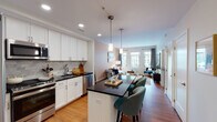 This single-floor residence offers a thoughtfully designed open-concept layout that seamlessly connects the kitchen, dining, and living areas. The kitchen is a standout feature, outfitted with crisp white cabinetry, dark granite countertops, a classic subway tile backsplash, and a full suite of stainless steel appliances including a gas range, microwave, refrigerator, and dishwasher. A central island with a matching dark countertop provides additional prep space and casual seating with teal upholstered barstools. Pendant lighting above the island adds a refined touch. Warm hardwood flooring flows consistently throughout the entire space, enhancing continuity between rooms.

The living area is bright and inviting, benefiting from a large multi-pane window that frames urban views and fills the room with natural light. The bedroom is comfortably proportioned, featuring a ceiling fan, a window with city views, hardwood floors, and direct access to a closet. An adjacent bathroom showcases a white vanity with granite countertops, a large mirror, and classic black-and-white mosaic tile flooring. The overall ambiance is clean, modern, and functional.
