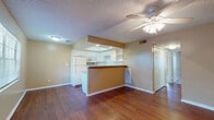 This single-floor residence is designed with a practical, open layout that connects the living and kitchen areas seamlessly. The living space features warm-toned hardwood flooring that extends throughout the main area, complemented by neutral beige walls and a textured ceiling. A ceiling fan with a light fixture is centrally installed, providing both airflow and ambient lighting.

The kitchen is positioned behind a raised peninsula-style breakfast bar, creating a natural visual divider without closing off the space. White cabinetry lines the kitchen walls, offering generous storage, while a recessed ceiling above the kitchen workspace adds architectural interest. White appliances, including a full-size refrigerator, built-in microwave, and dishwasher, are included alongside a sink with ample counter space.

The bedrooms are carpeted and feature ceiling fans, neutral walls, and six-panel doors leading to closets. One bedroom includes a window with vertical blinds, allowing natural light into the space. The bathroom is clean and functional, finished with light tile flooring and a full tub-shower combination. Throughout the residence, consistent neutral tones and white trim create a cohesive, move-in-ready aesthetic.
