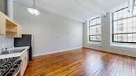 Located at 166 Valley St in Providence, Rhode Island, this single-floor loft-style unit reflects the character of an adaptively reused industrial building. The open-plan living area is defined by warm, richly toned original hardwood floors that run throughout, contributing a sense of historic authenticity. Soaring ceilings with exposed structural beams and visible ductwork reinforce the industrial aesthetic, while large arched windows with multi-pane frames allow abundant natural light to fill the space and offer views of the surrounding urban streetscape. The painted brick surround framing the windows adds further architectural interest.

The kitchen is efficiently arranged along one wall and features light wood cabinetry, light-toned countertops, a stainless steel gas range, dishwasher, refrigerator, and a single-basin sink. An exposed HVAC duct runs overhead, consistent with the building's industrial design language. A separate enclosed area accommodates a bedroom and a full bathroom, which includes tile flooring, a tub-shower combination, a vanity with wood cabinetry, and clean neutral finishes throughout. The overall ambiance balances historic industrial character with functional, updated living amenities.