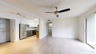This single-floor residence offers a well-organized layout with a clean, neutral aesthetic throughout. The open living area is finished with light wood-look flooring and features a ceiling fan overhead, creating a bright and airy atmosphere. A sliding glass door leads to a private balcony, allowing natural light to fill the space while providing views of the surrounding greenery.

The kitchen is positioned adjacent to the living area in a semi-open arrangement, outfitted with white upper cabinetry, two-tone gray lower cabinets, and a full suite of stainless steel appliances including a refrigerator, electric range, microwave, and dishwasher. Light countertops and a flush-mount ceiling light complete the functional space. A walk-in pantry or storage closet with wire shelving is conveniently located nearby.

The bedrooms are carpeted for comfort and each include ceiling fans and closet storage with louvered bifold doors. One bedroom features a window with blinds providing additional natural light. A dedicated laundry area houses a full-size washer and dryer beneath overhead white cabinetry. The bathroom includes a tub-shower combination, a white vanity with stone-look countertop, and wood-look tile flooring, finished with brushed nickel hardware throughout.